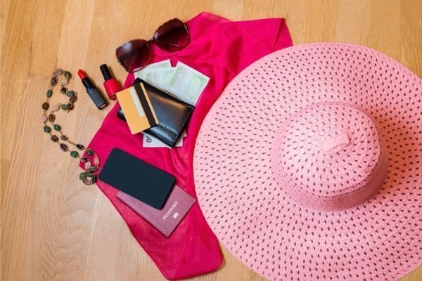 Things that can go in a wallet phone case like a passport, ID, credit cards, etc., spread out on the floor with a pink hat and sunglasses