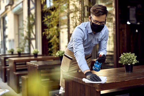 Server wearing a mask and a restaurant server apron while cleaning a table