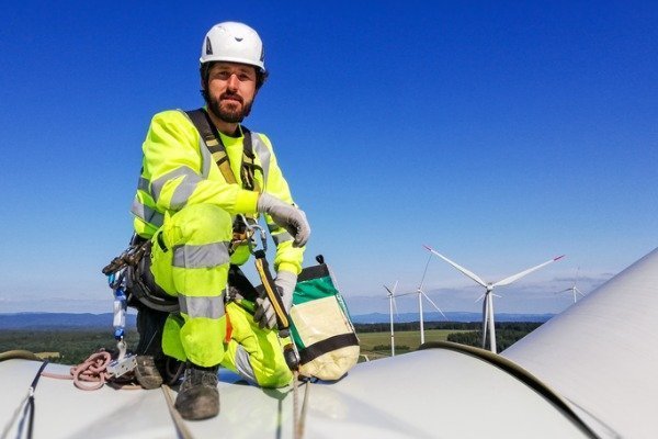 worker-wearing-safety-gear-kneeling-on-enormous-onshore-wind-turbine
