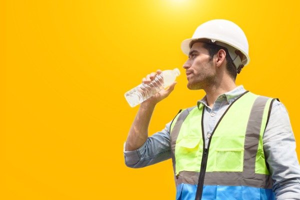 worker-wearing-a-protective-clothing-and-helmet-while-drinking-water-in-summer-warehouse-work-concept